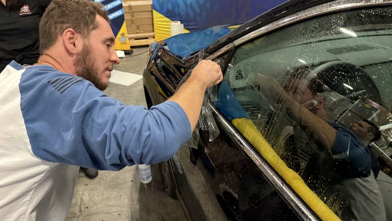 Detailer taping trim on a black vehicle before machine polishing